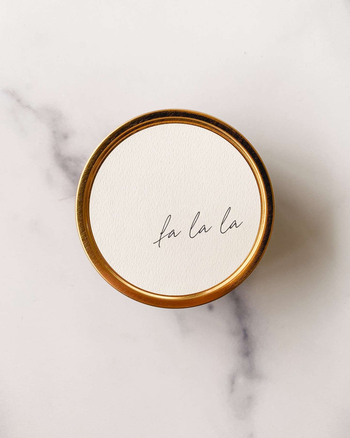 Round container with 'fa la la' text on a marble surface