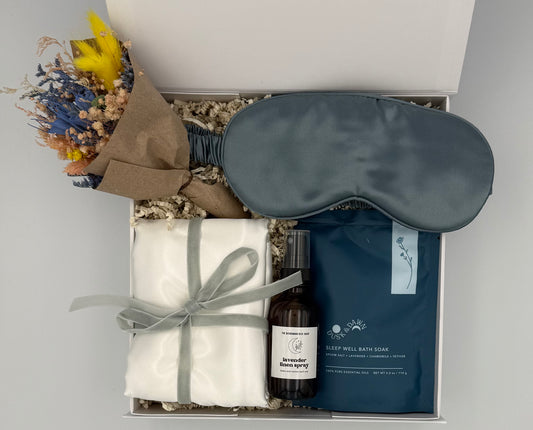Gift set with eye mask, bath soap, and towel in a box on a light gray background