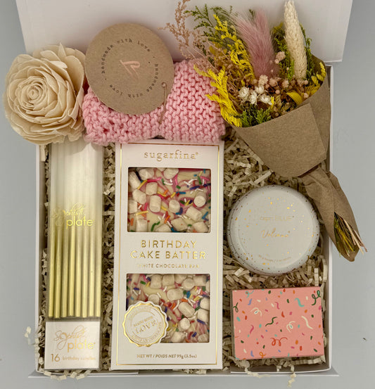 Gift box with birthday cake batter, candles, and decorative items on a gray background