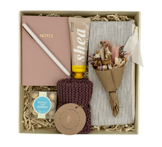 Gift box containing a notebook, lip balm, hand towel, and other items on a white background