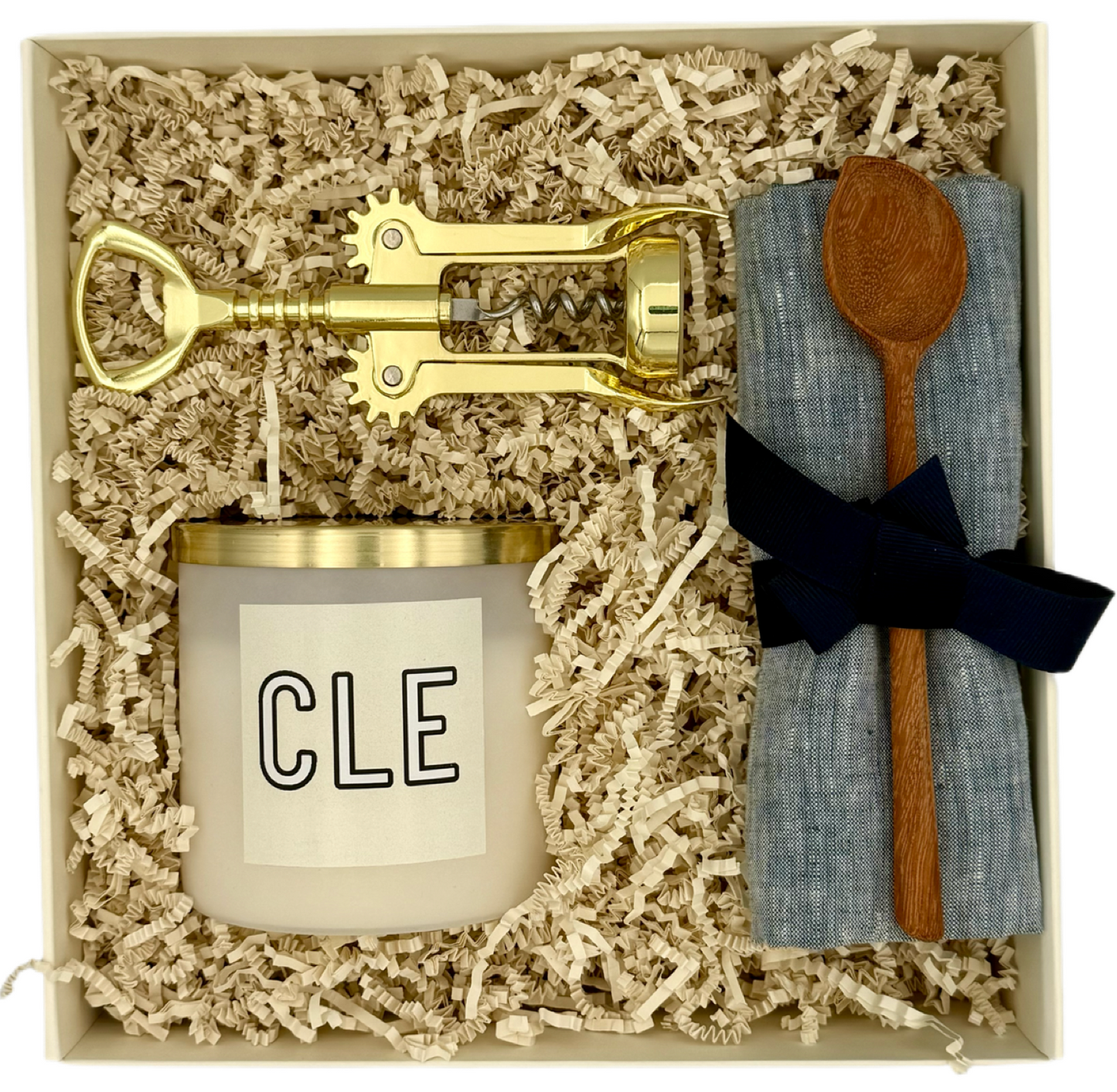 Set of gold corkscrew, candle labeled 'CLE', wooden spoon, and blue napkin in a box.