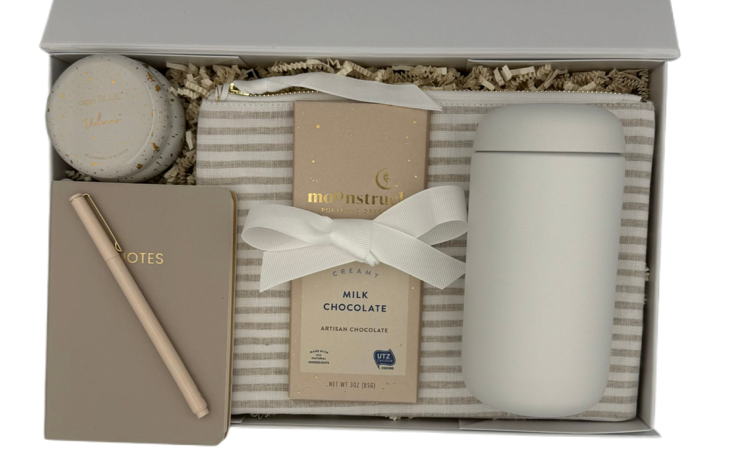 Gift set with a notebook, chocolate bar, and candle in a decorative box.