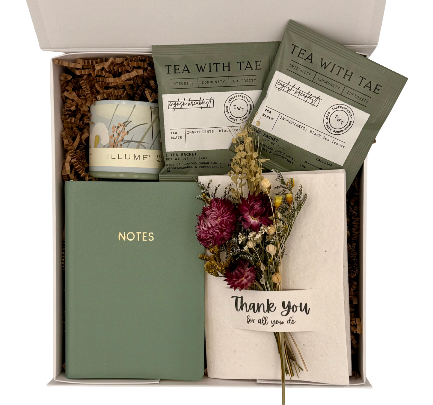 Gift box with tea, candle, notebook, and flowers on a white background