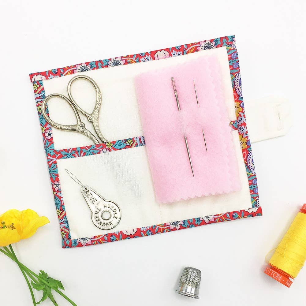 Sewing kit with scissors, thread, and pins on a floral-patterned mat.