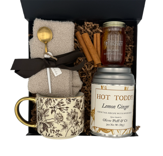 Gift set with mug, tea canister, honey, and cinnamon sticks in a box.