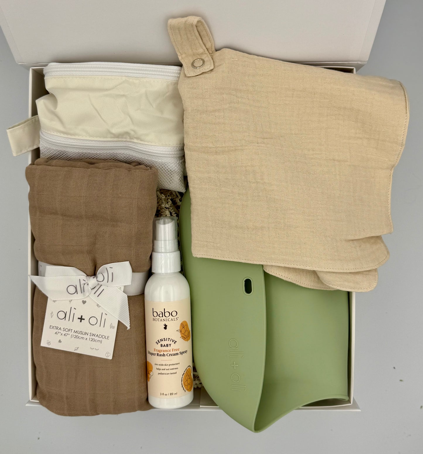 Box containing baby clothes and products with visible brand labels on a gray background