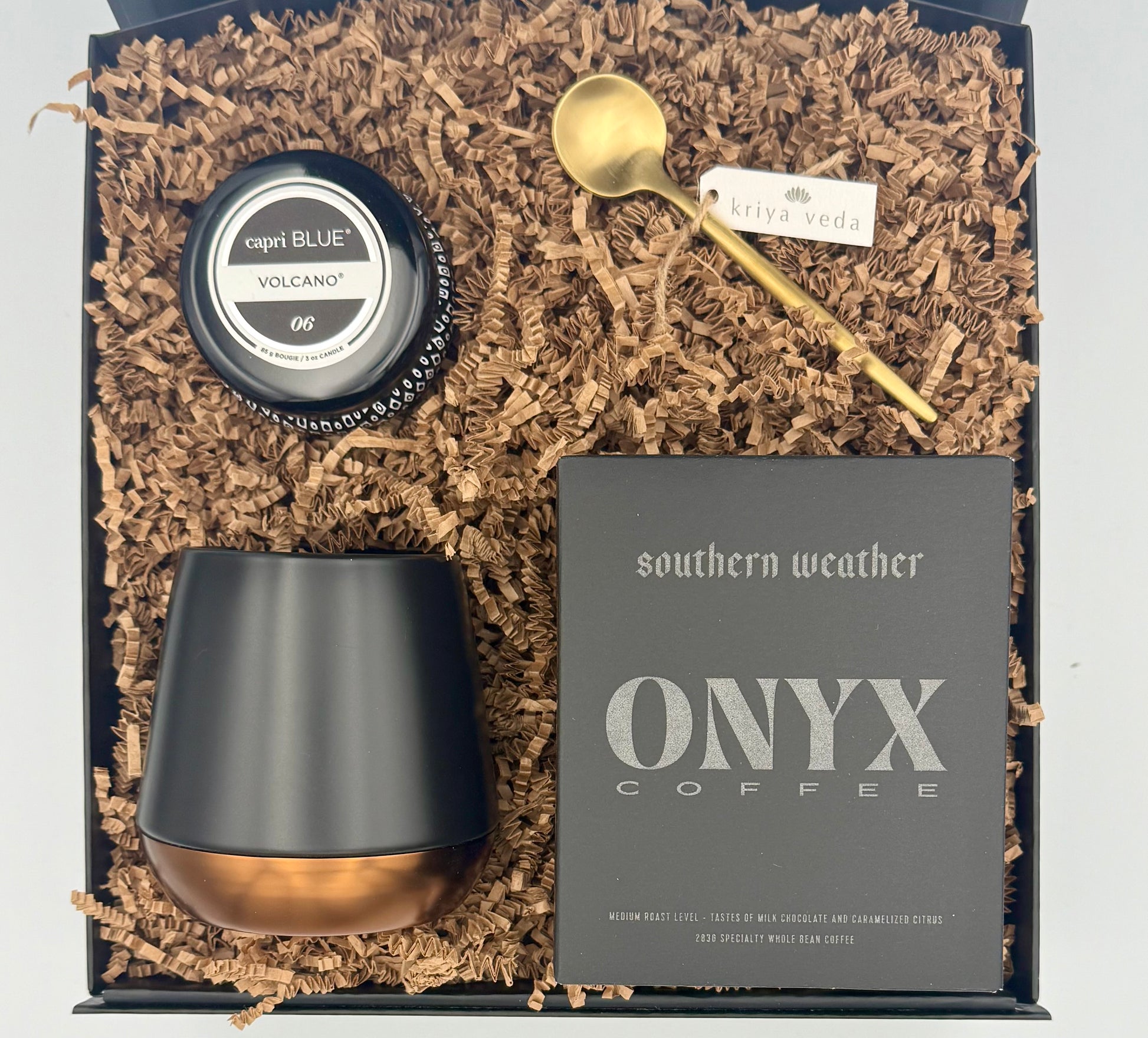 Gift set with ONYX coffee packaging, black and gold cup, and small container on crinkled brown paper.
