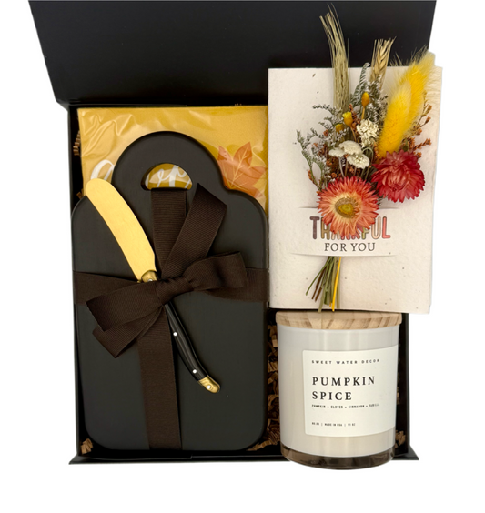 Gift set with a pumpkin spice candle, floral arrangement, and black box with a bow.