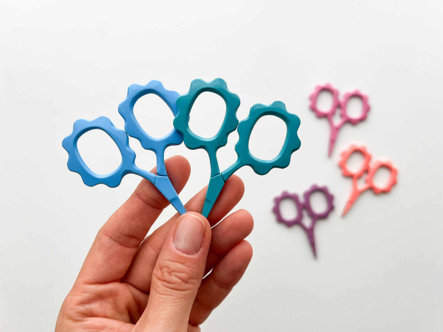 Colorful toy scissors held by a hand with more scissors in the background on a light gray background