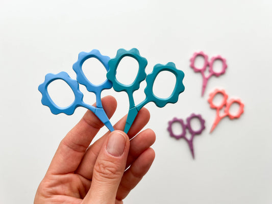 Colorful toy scissors held by a hand with more scissors in the background on a light gray background