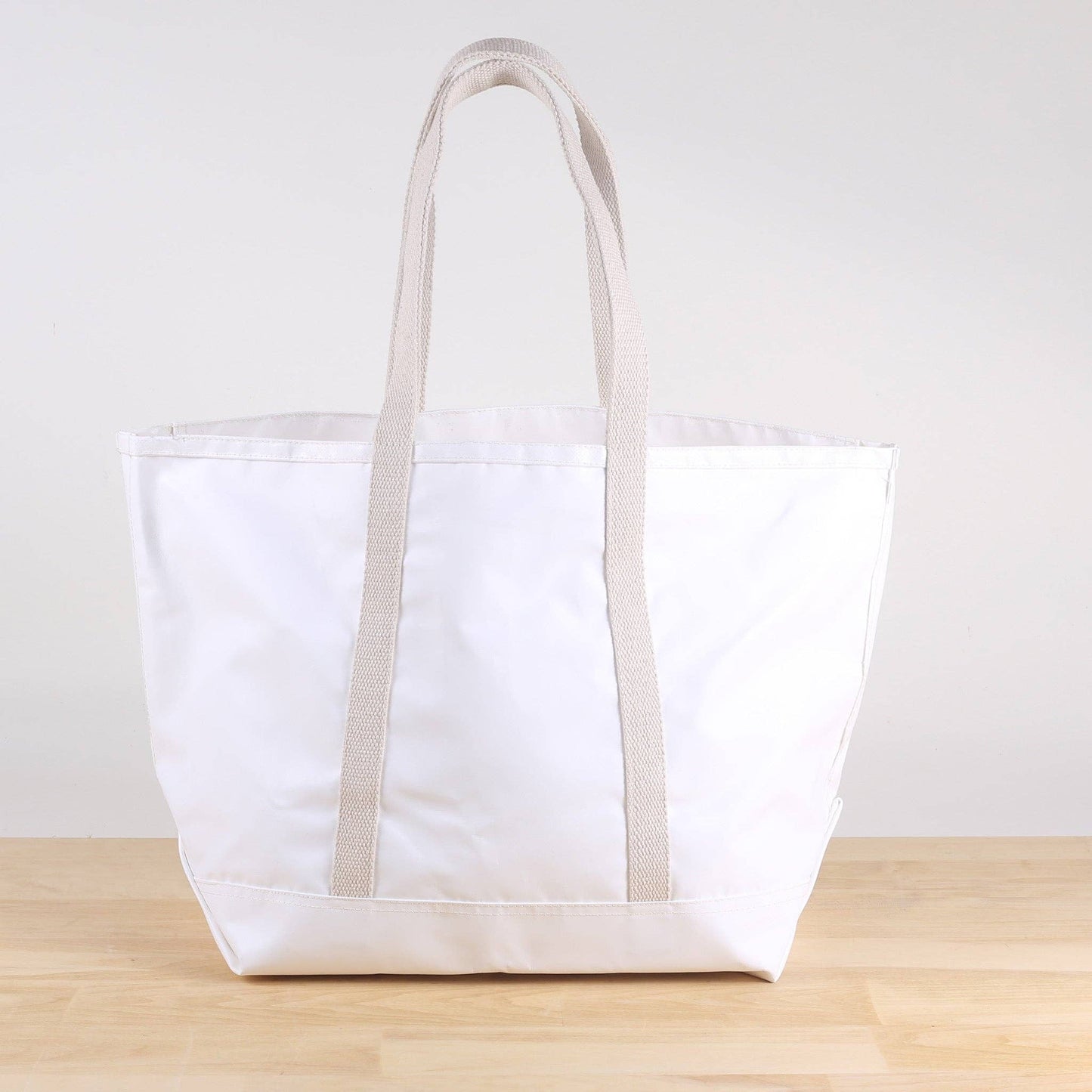 White tote bag with beige handles on a wooden surface and light gray background