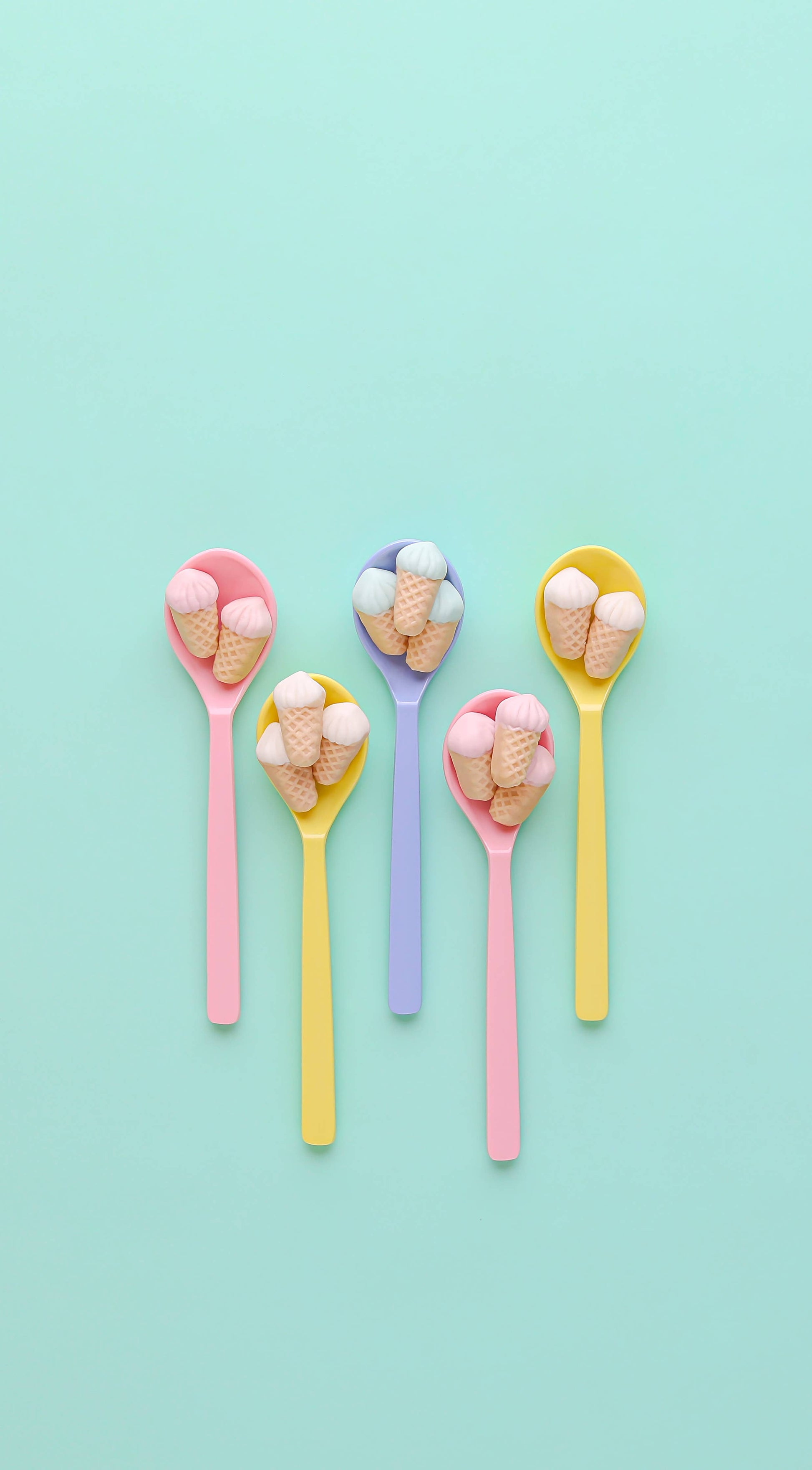 Five colorful spoons with ice cream cones on a light blue background