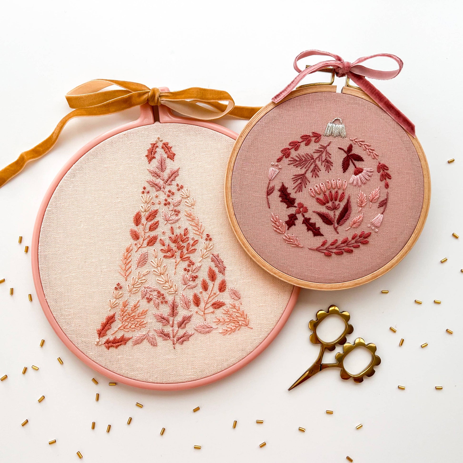 Two embroidery hoops with floral patterns on a white background with gold accents.
