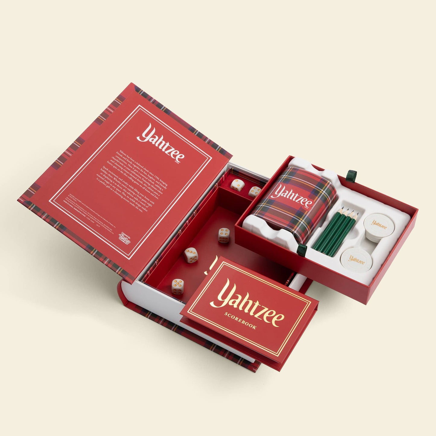 An open red and black plaid Yahtzee game box showing the included contents, including dice, green pencils, white cups, and a plaid bandana, on a light beige background.