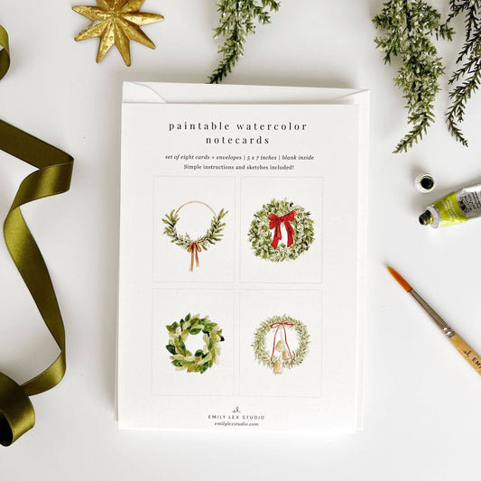 Paintable watercolor notecards with Christmas wreath designs on a white background with decorative items.