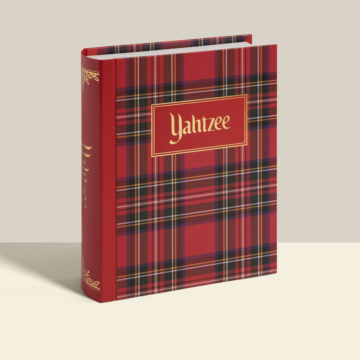 A hardcover book titled 'Yahtzee' with a red plaid cover and gold lettering, standing upright against a light beige background.