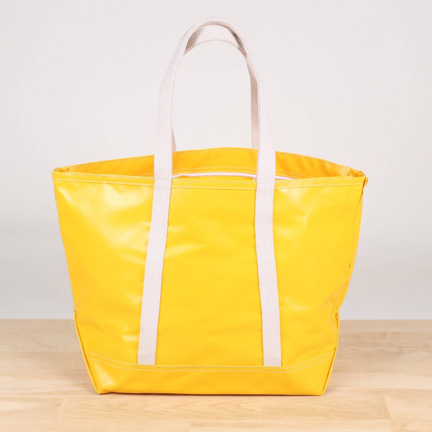 Yellow tote bag with white straps on a wooden surface and light gray background