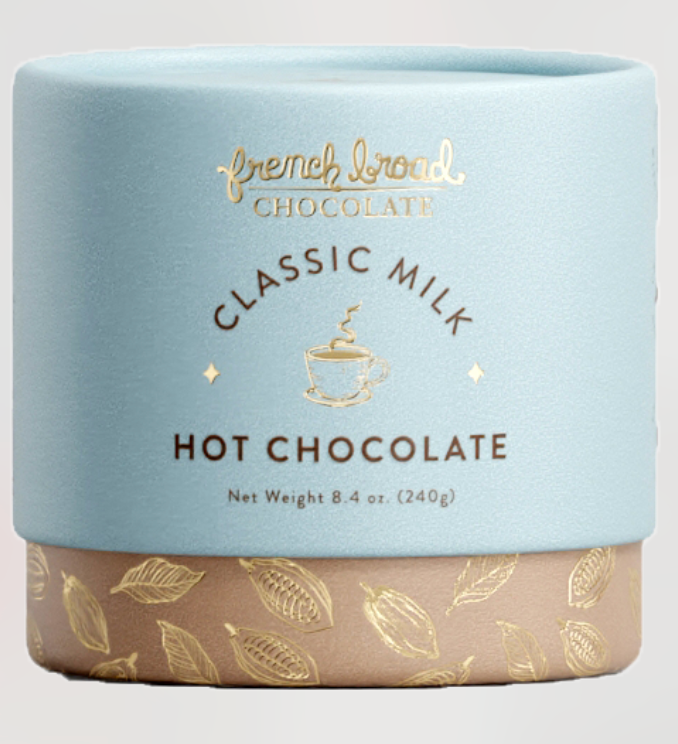 Container of French Broad Classic Milk Hot Chocolate with gold text and leaf patterns on a light gray background