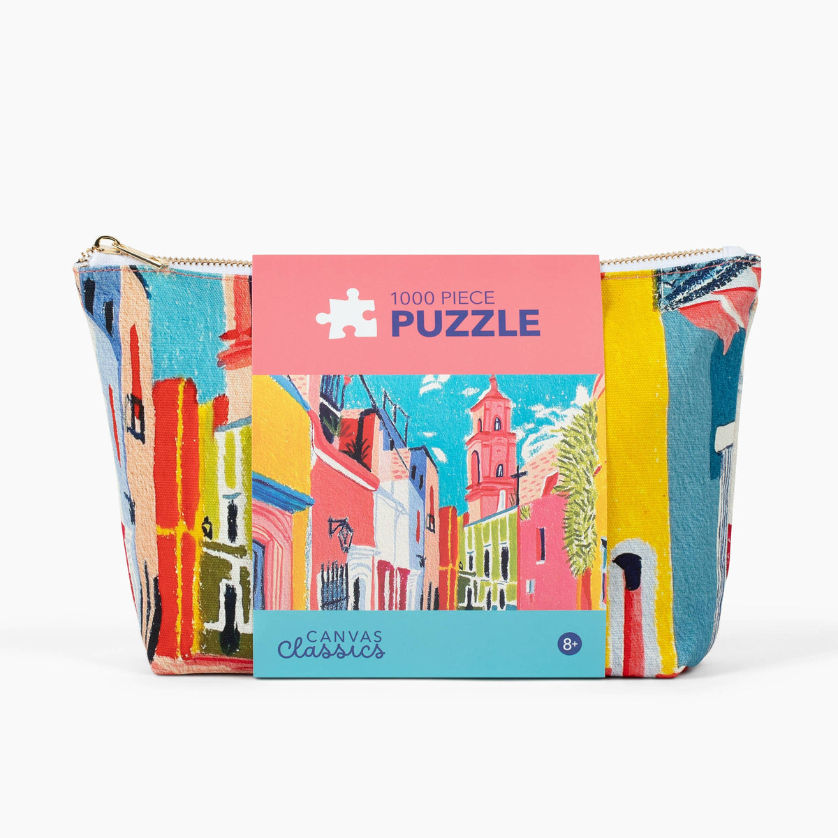 A colorful 1000-piece jigsaw puzzle by Canvas Classics, featuring an artistic depiction of a European street with buildings in pink, yellow, blue, and red. The puzzle is shown with its packaging band, which is pink with a white puzzle icon and blue text reading '1000 PIECE PUZZLE'.