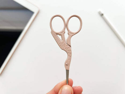 Small pink scissors held by a hand on a white background