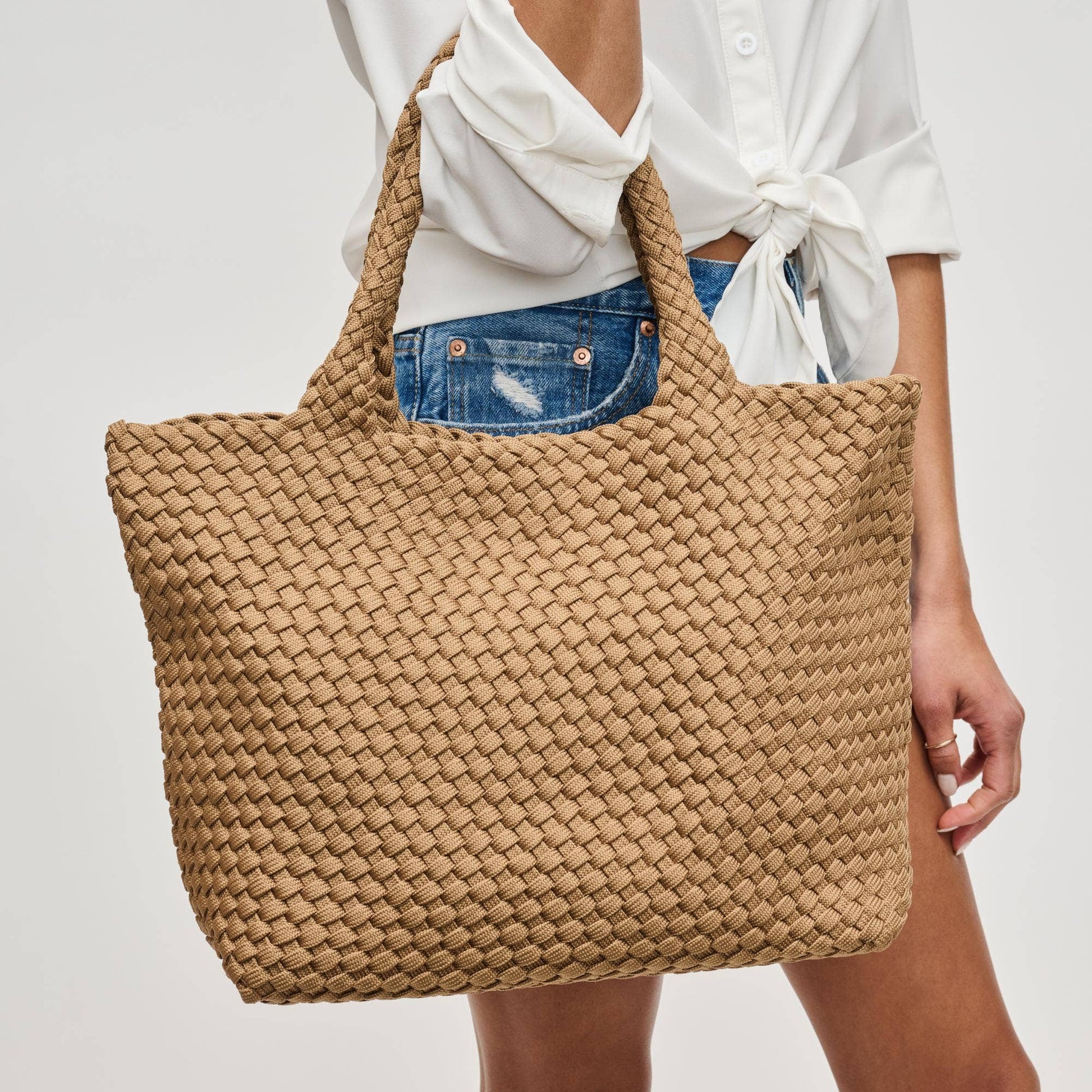 Person holding a woven beige tote bag against a plain background