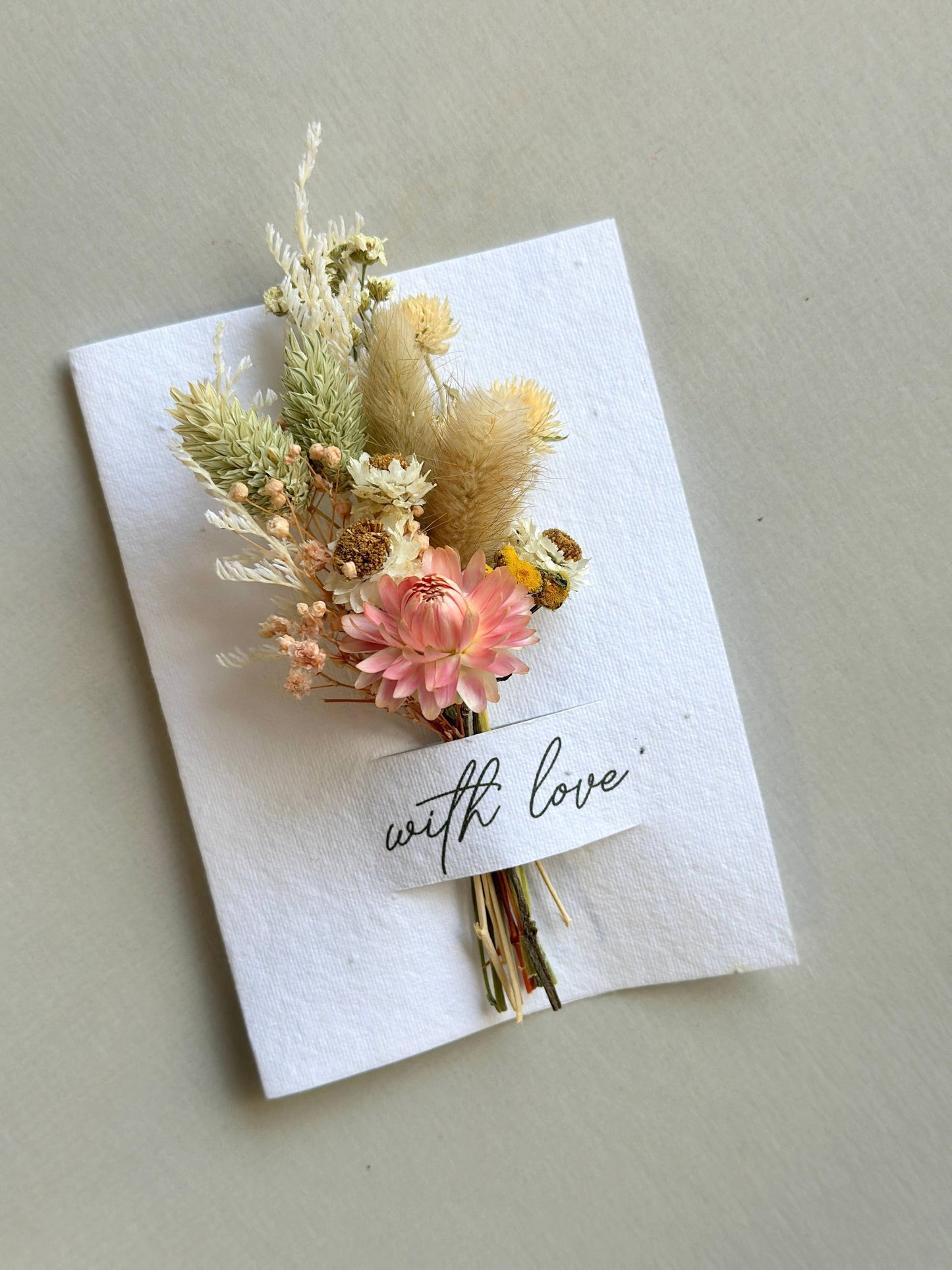 Small bouquet of dried flowers on a white card with 'with love' text, against a light gray background