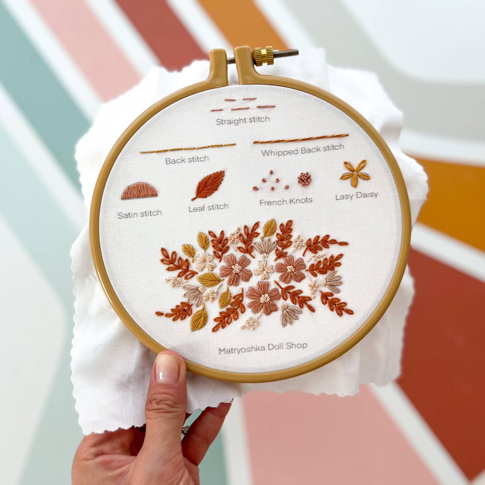 Embroidery hoop with floral design and stitch instructions against a colorful geometric background