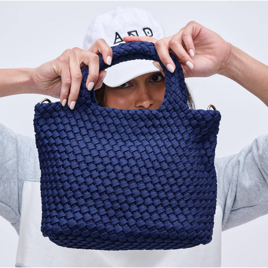 Person holding a blue woven handbag with a neutral background