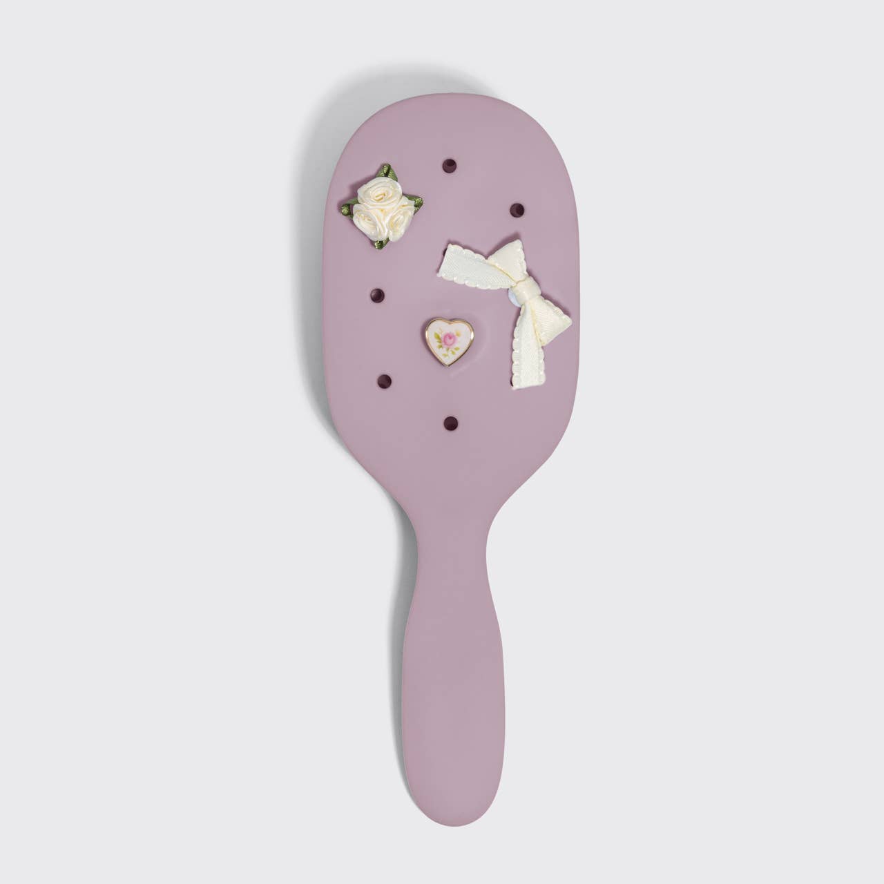 Purple hairbrush with decorative items on a light gray background