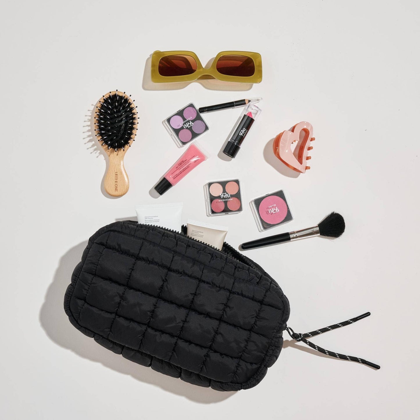 Black quilted makeup bag with cosmetic items on a light gray background