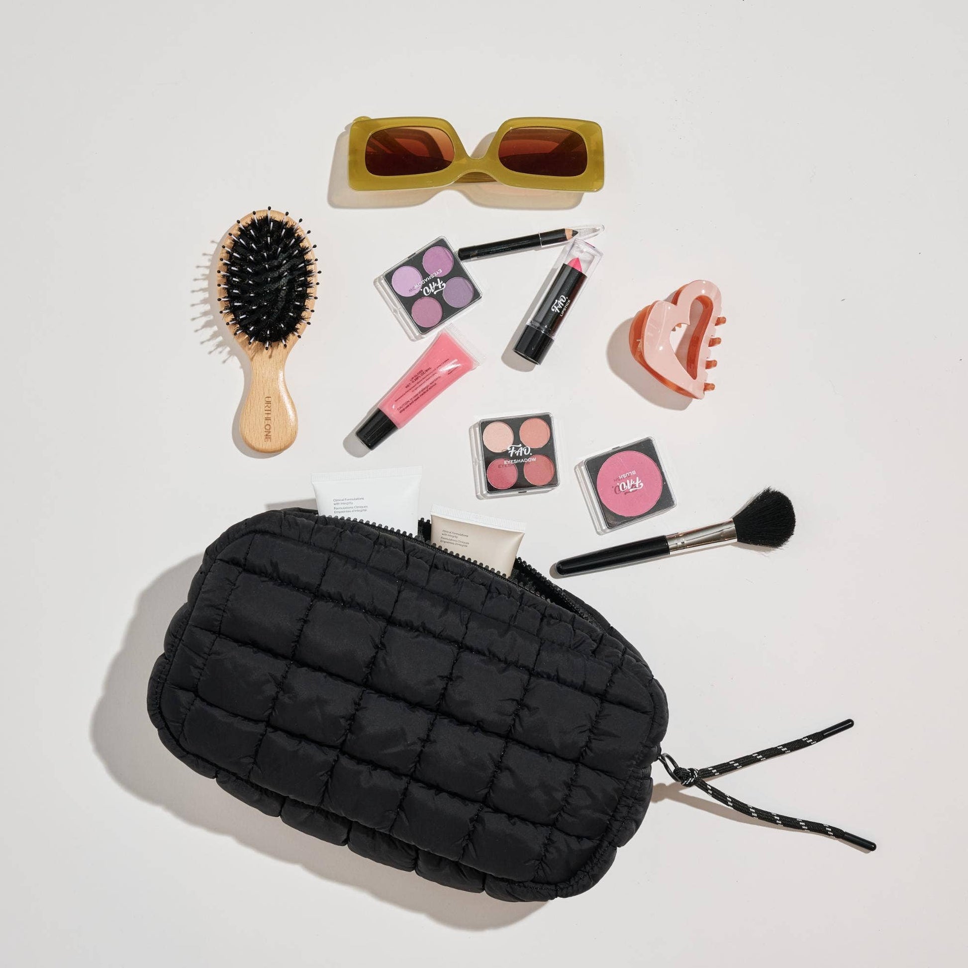 Black quilted makeup bag with cosmetic items on a light gray background