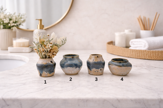 Four ceramic pots on a bathroom counter with decorative elements.
