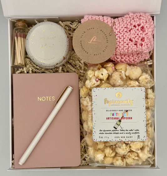 Gift box with a notebook, candle, pink knitted item, and popcorn.