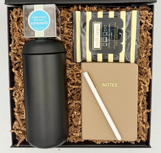 Gift set with black tumbler, notebook, pen, and caramels in a box.