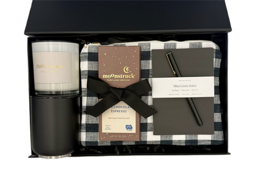 Gift set with candle, mug, plaid blanket, and notebook in a black box.