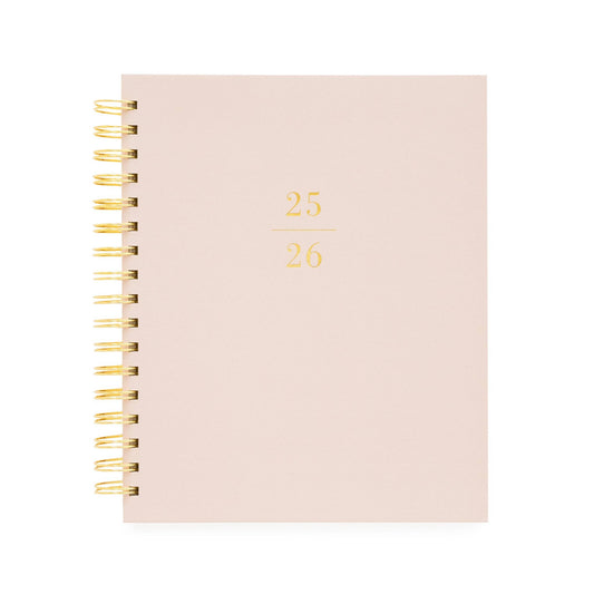Blush pink planner with gold spiral binding on a white background