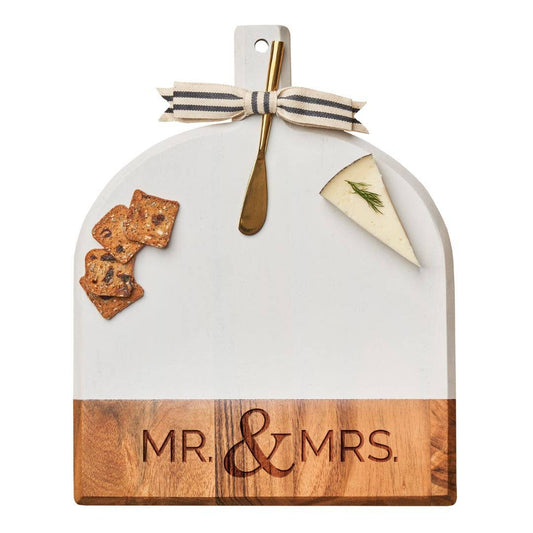 Decorative cutting board with 'MR. & MRS.' engraving, cheese, crackers, and a gold fork on a white background.