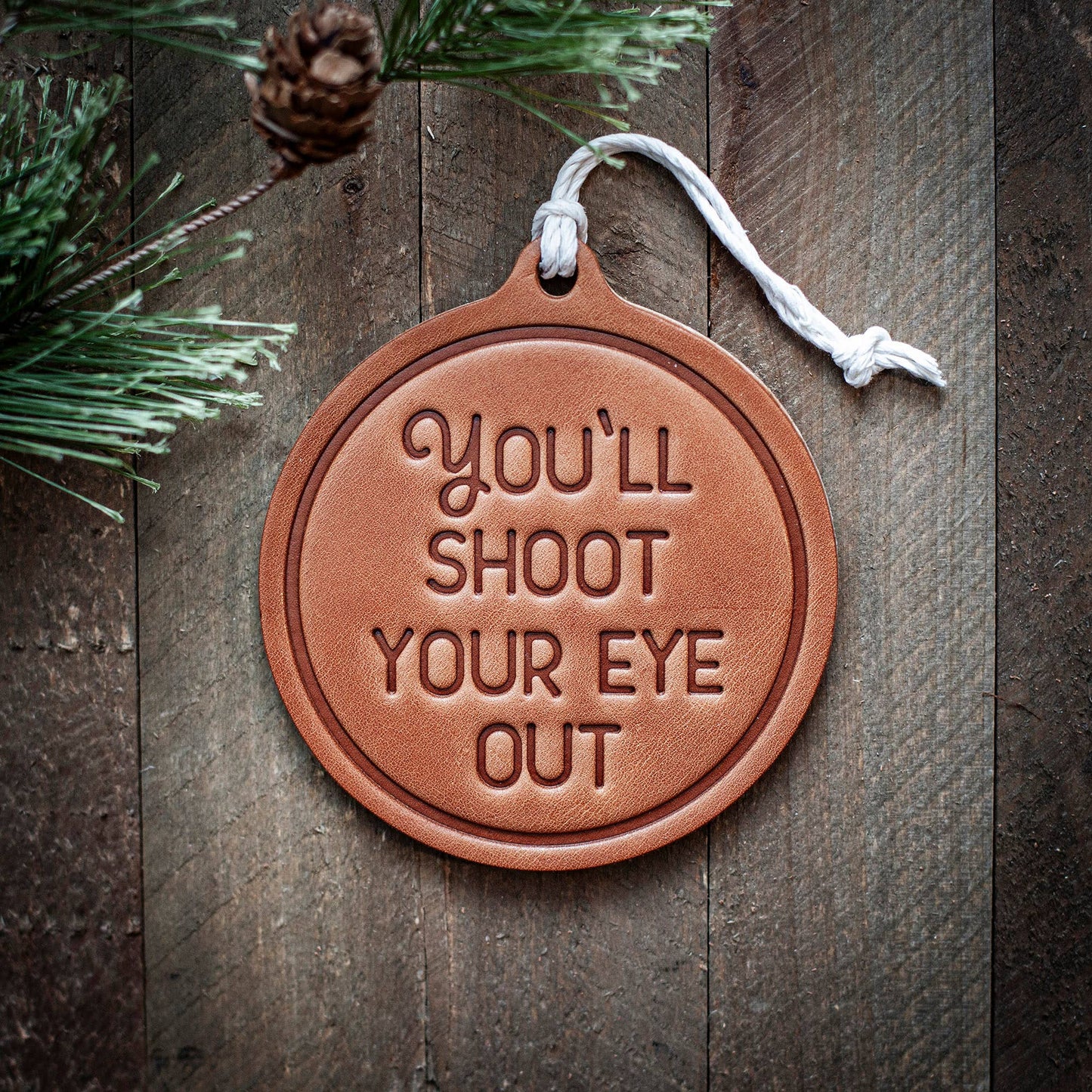 Brown leather ornament with 'You'll Shoot Your Eye Out' text on a wooden background