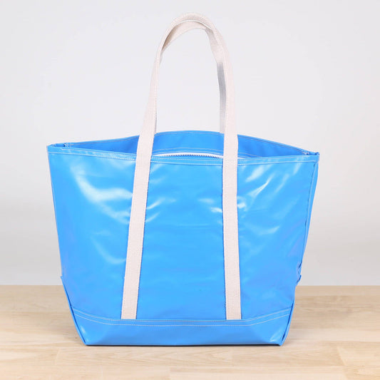 Blue tote bag with white handles on a light wooden surface and white background