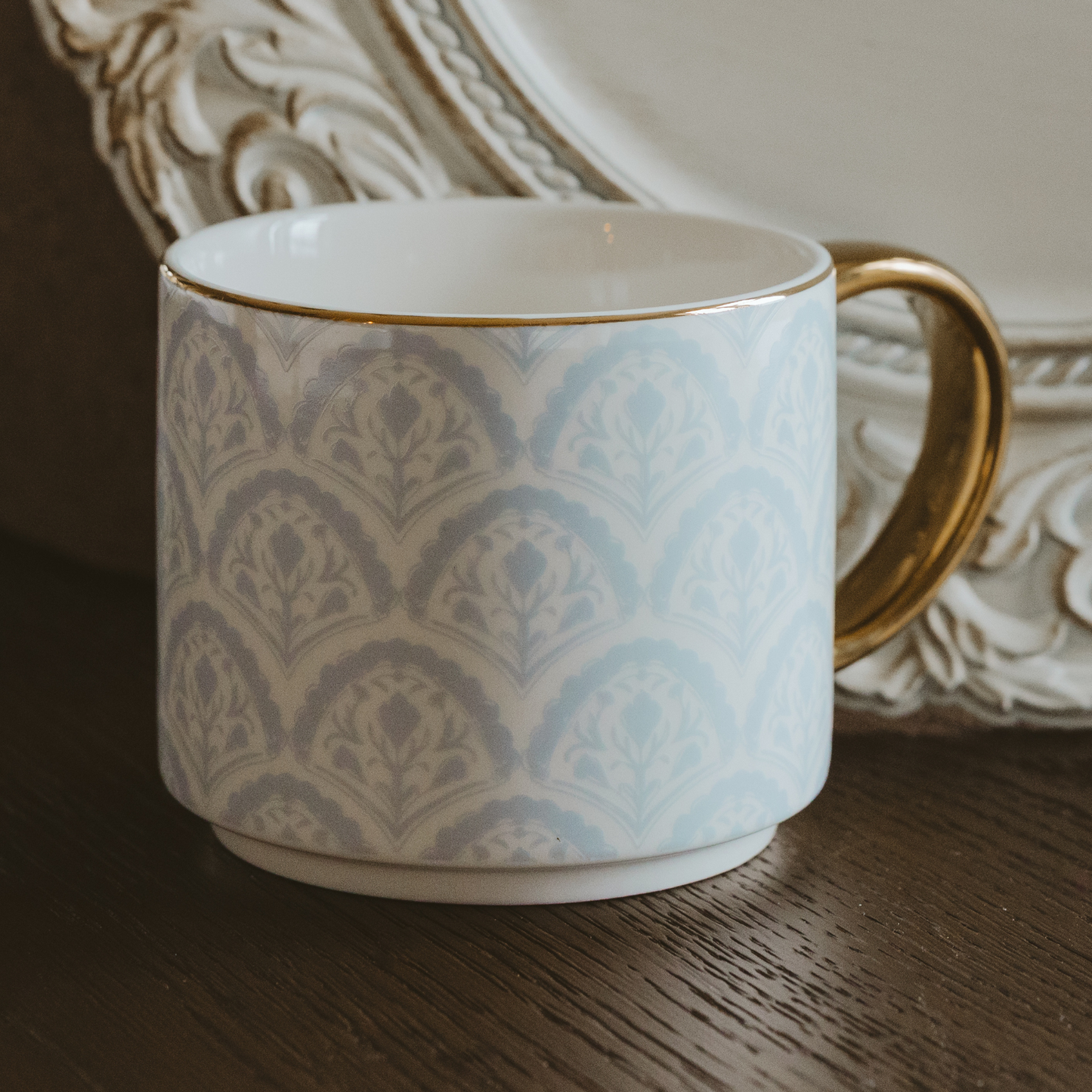 Ceramic mug with decorative pattern and gold handle on a wooden surface