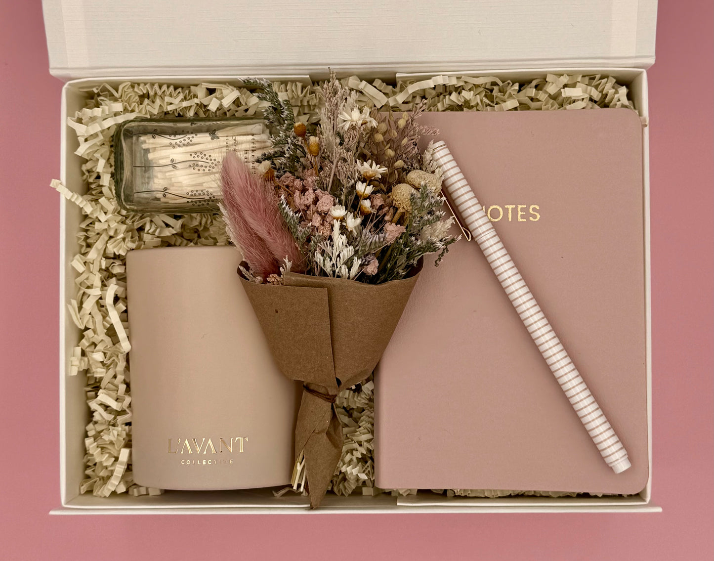 Gift set with a bottle, notebook, pen, and dried flowers in a box.