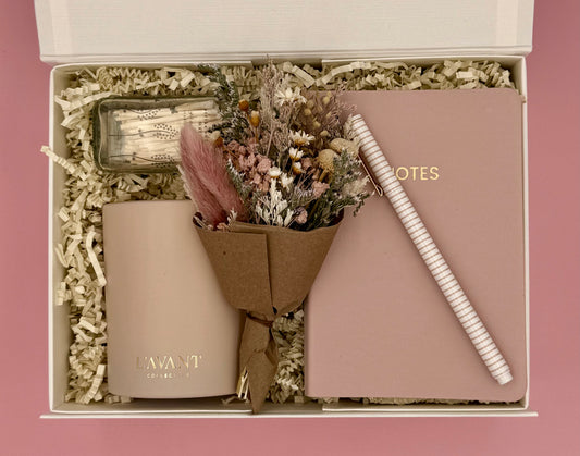 Gift set with a bottle, notebook, pen, and dried flowers in a box.