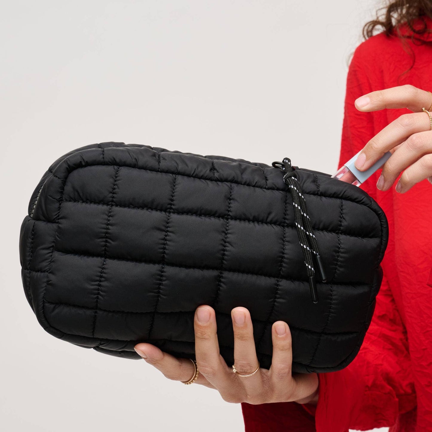 Person holding a black quilted pouch against a neutral background