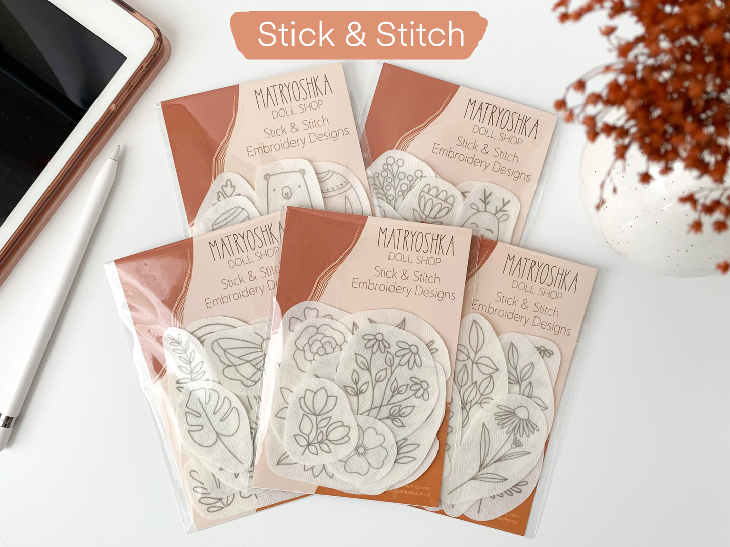 Matryoshka Doll Shop Stick & Stitch embroidery designs on a white surface with a phone and dried flowers.