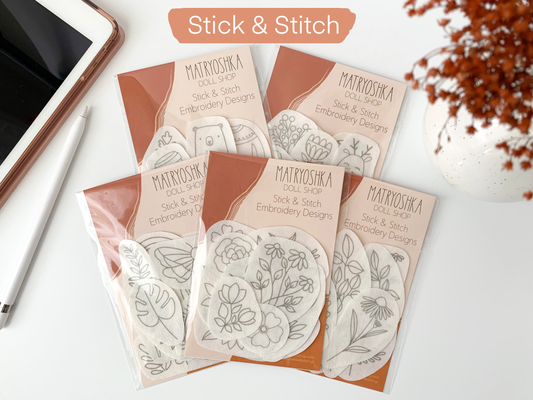 Matryoshka Doll Shop Stick & Stitch embroidery designs on a white surface with a phone and dried flowers.