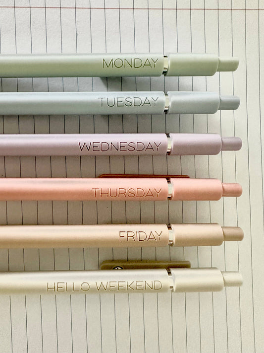 Set of pens labeled for each day of the week on a lined notebook background