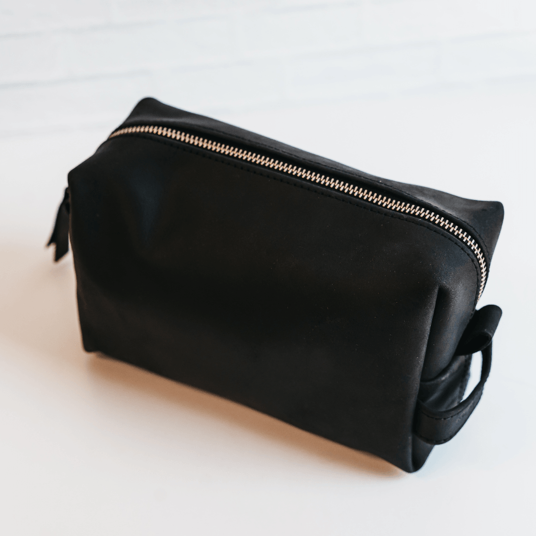 Black toiletry bag with a gold zipper on a light background