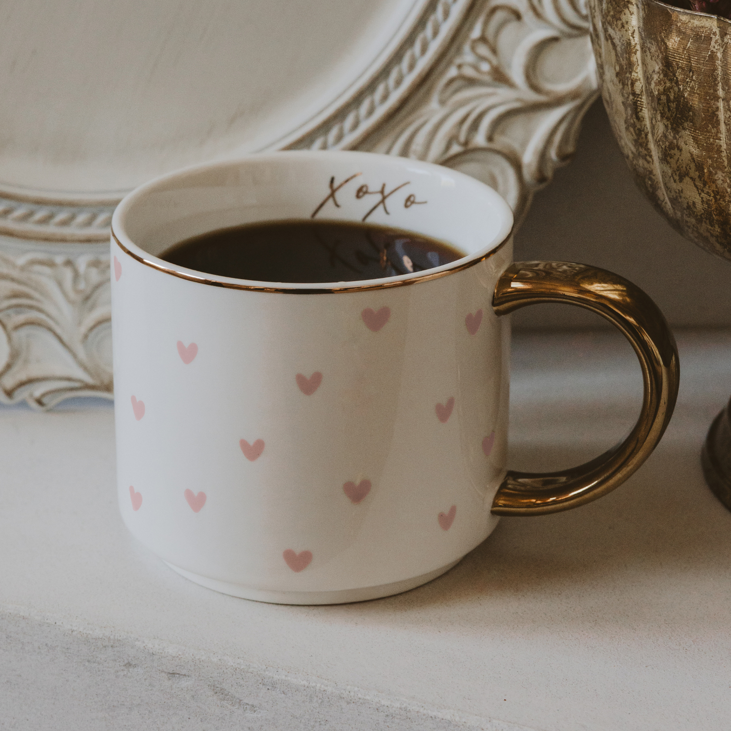 White mug with pink heart patterns and gold handle on a surface