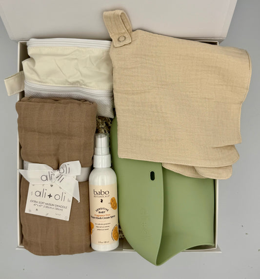 Box containing baby clothes and products with visible brand labels on a gray background