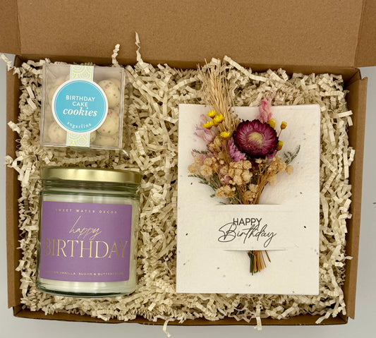Gift box with birthday candle, cookies, and a card with flowers on a white background